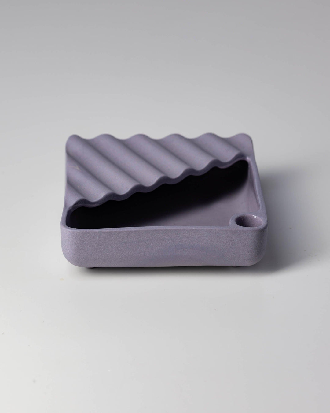 Lavender ceramic ashtray with wavy design on a grey background.