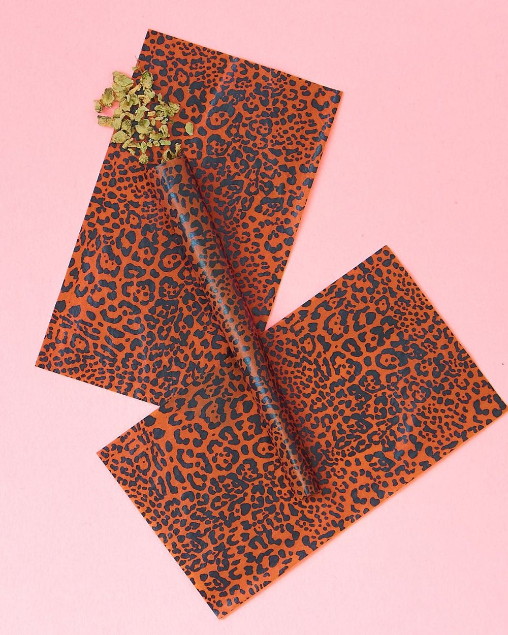 Leopard print rolling papers with joint and buds on a pink background.
