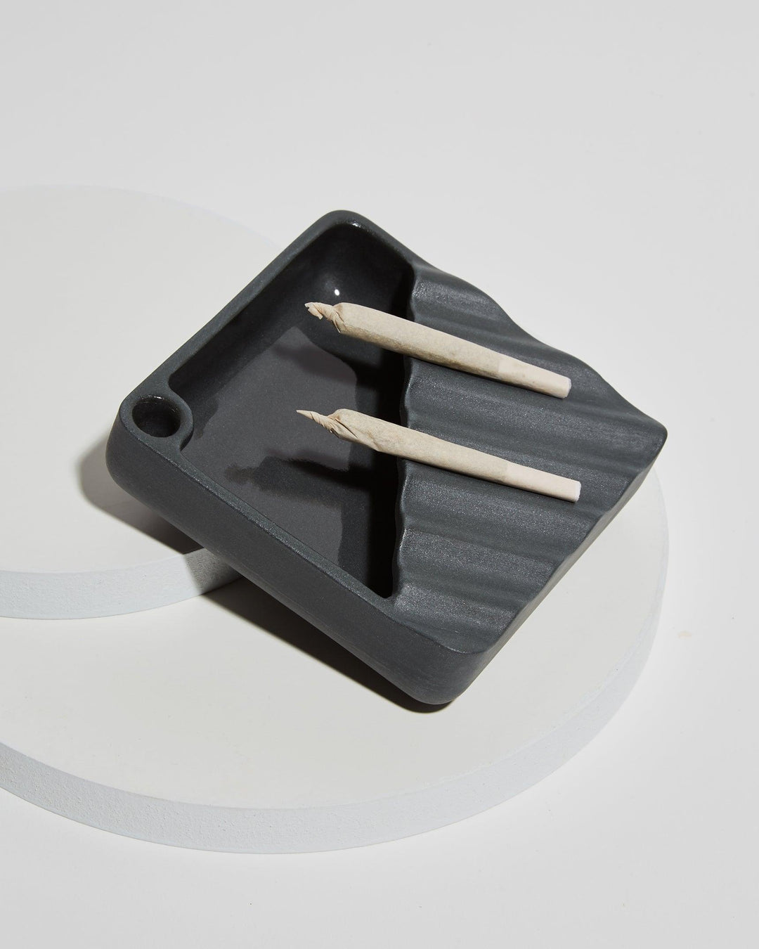 Two cannabis joints resting on a black ceramic ashtray. 