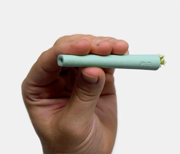 Man holding mint green ceramic one-hitter with bowl filled with herbs.