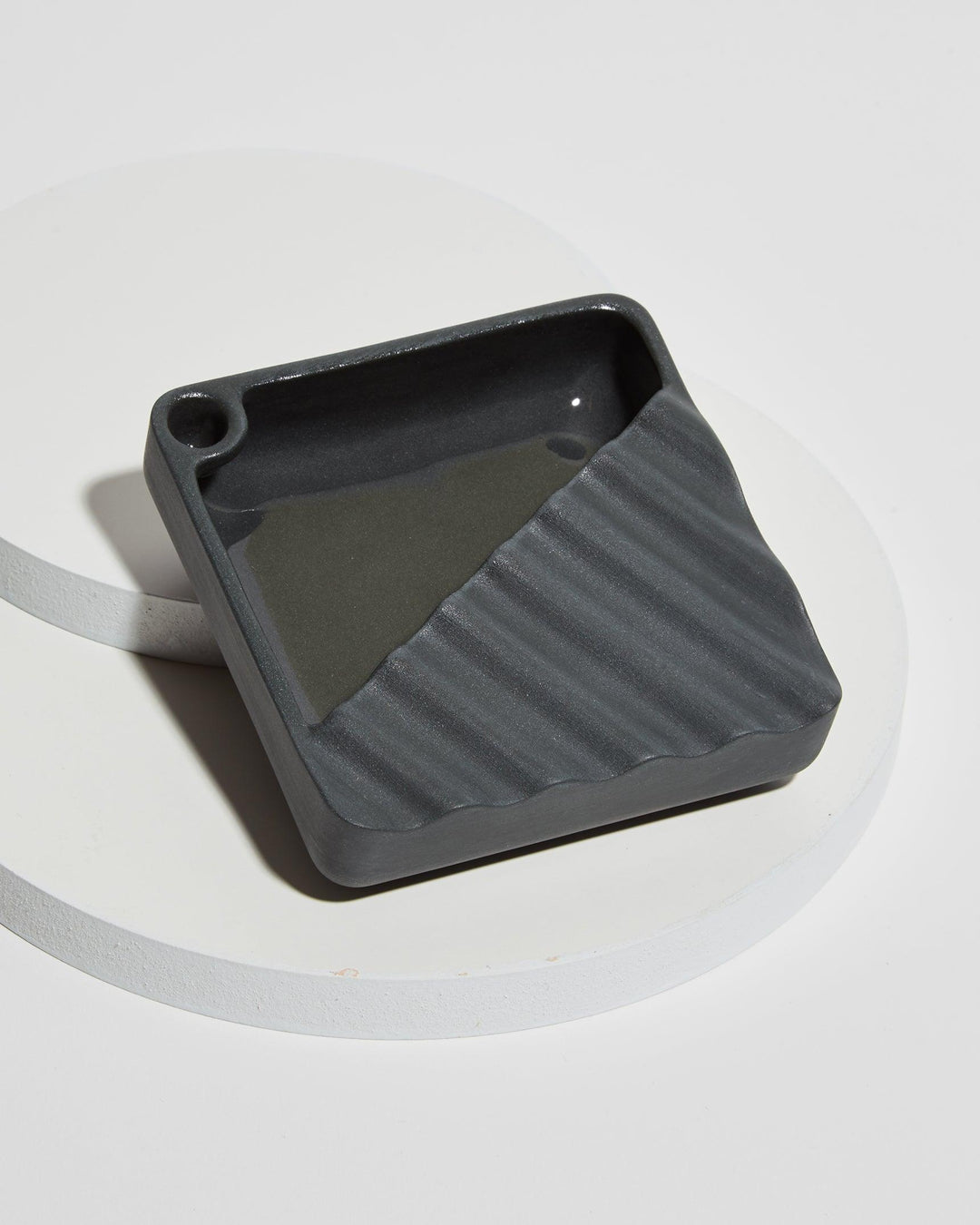 Ceramic ashtray with wavy design in color black.